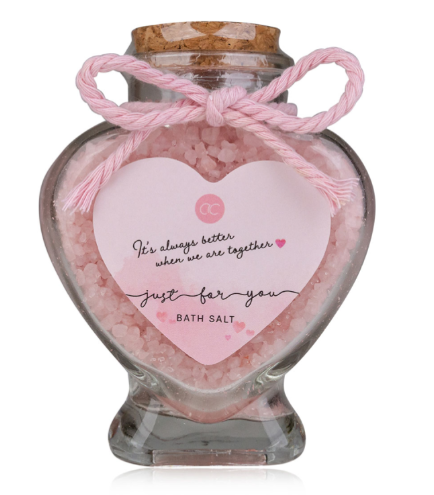 Glass jar filled with pink bath salts and a heart-shaped tag on a white background